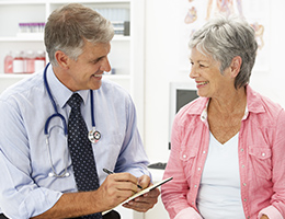 Woman and a doctor in an exam room, smiling at each other.